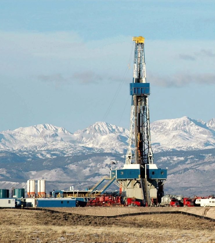 A drilling rig working below the snow-covered Wind River Range